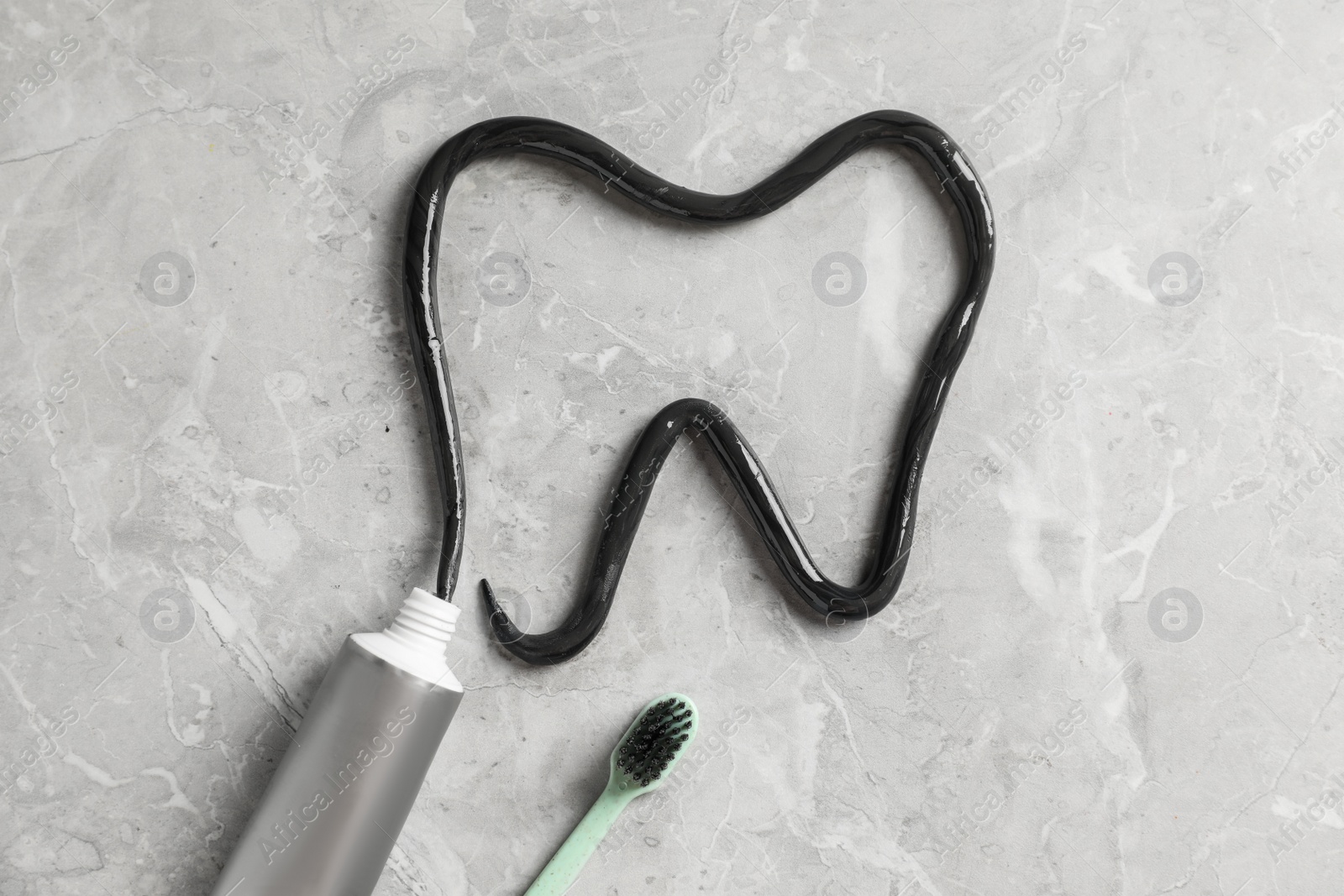 Photo of Tooth drawn with charcoal toothpaste on light grey table, flat lay