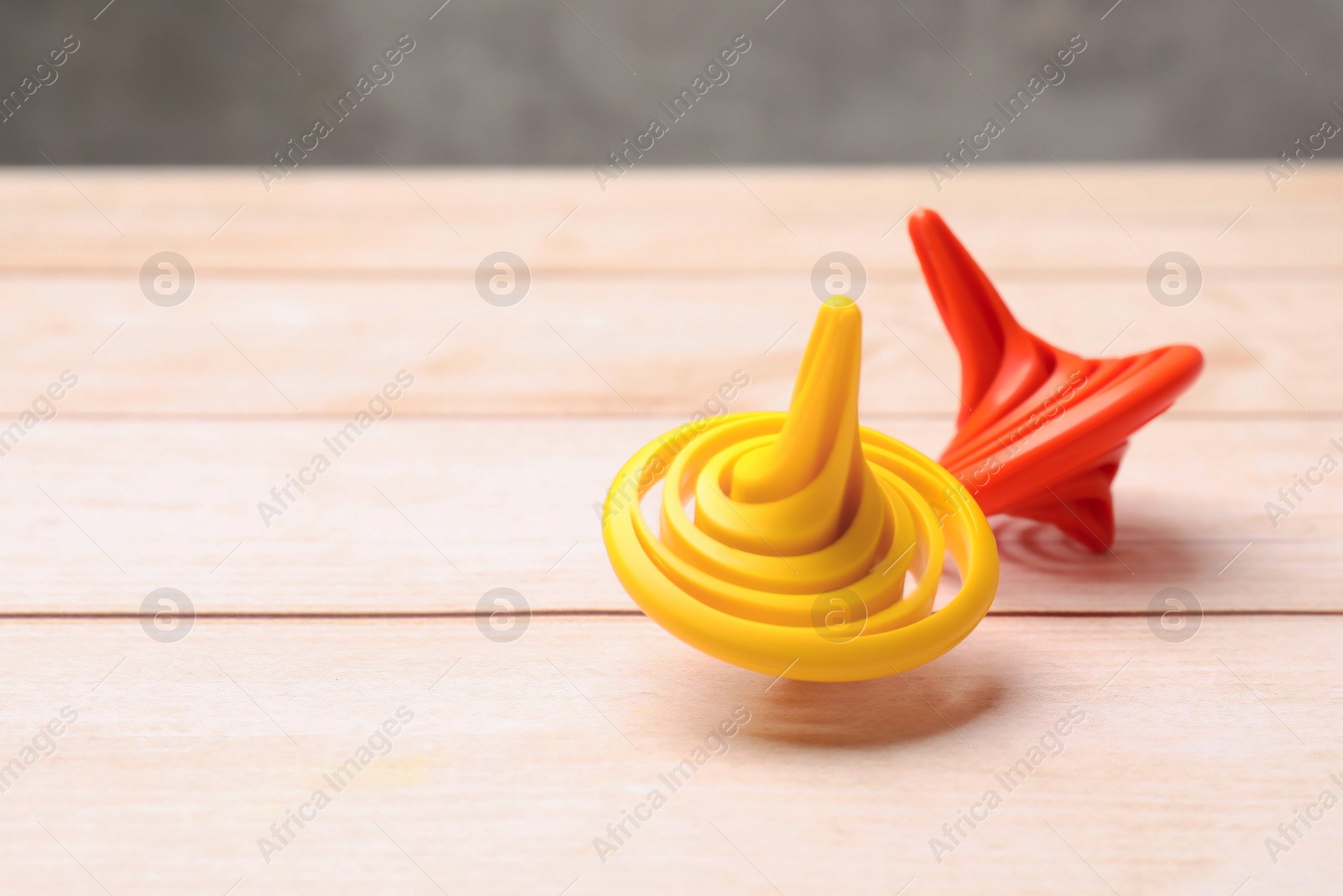 Photo of Bright spinning tops on light wooden table, closeup. Space for text