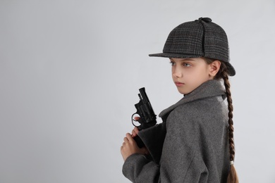 Photo of Cute little detective with revolver on grey background. Space for text