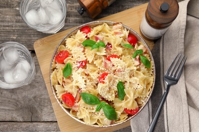 Delicious pasta with tomatoes, basil and parmesan cheese served on wooden table, flat lay