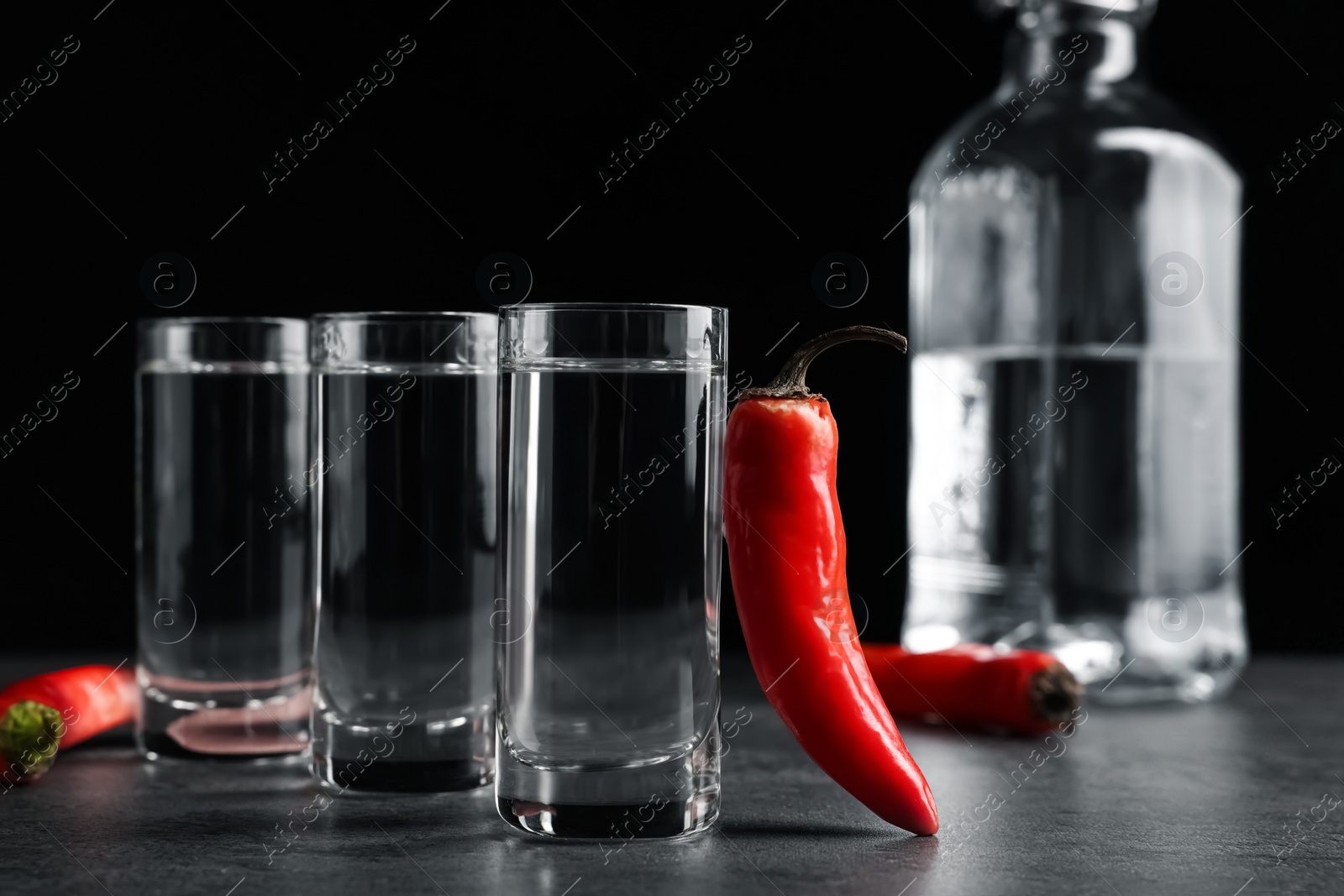 Photo of Red hot chili peppers and vodka on grey table against black background