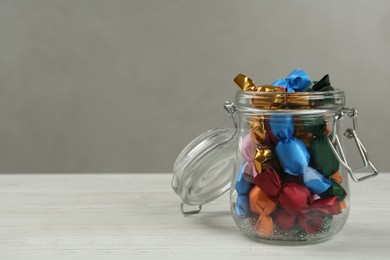 Photo of Candies in colorful wrappers on white wooden table. Space for text