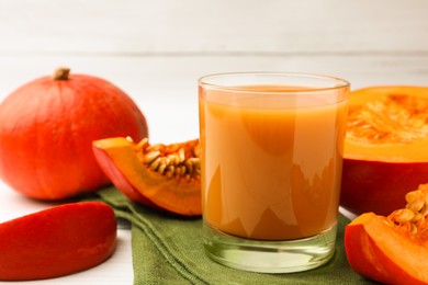 Tasty pumpkin juice in glass, whole and cut pumpkins on white wooden table. Space for text