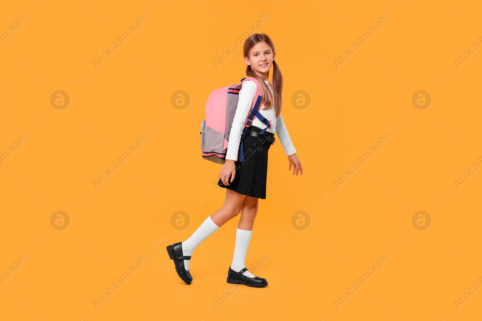 Photo of Happy schoolgirl with backpack on orange background
