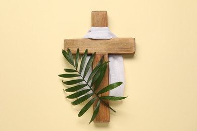 Photo of Wooden cross, white cloth and palm leaf on beige background, top view. Easter attributes