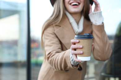 Young woman with cup of coffee on city street in morning, focus on hand