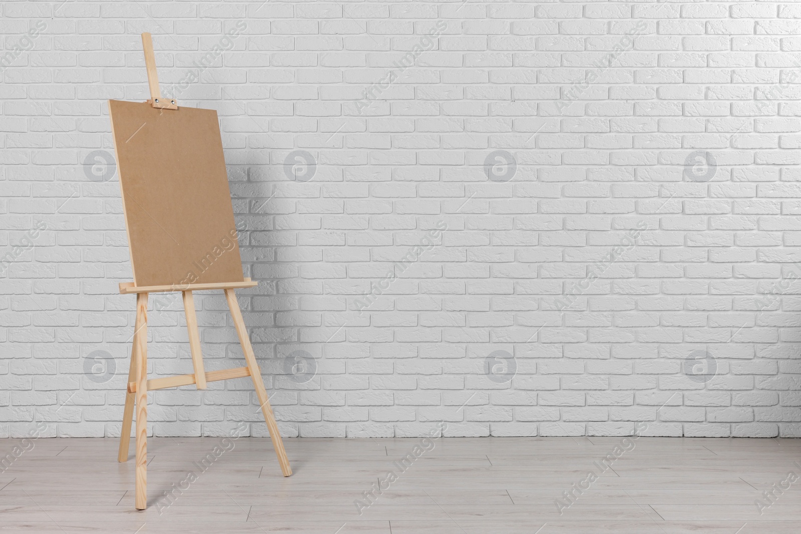 Photo of Wooden easel with blank board near white brick wall indoors. Space for text