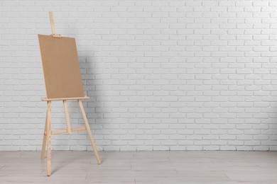 Photo of Wooden easel with blank board near white brick wall indoors. Space for text