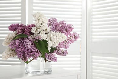 Beautiful lilac flowers in glass vase on white table. Space for text