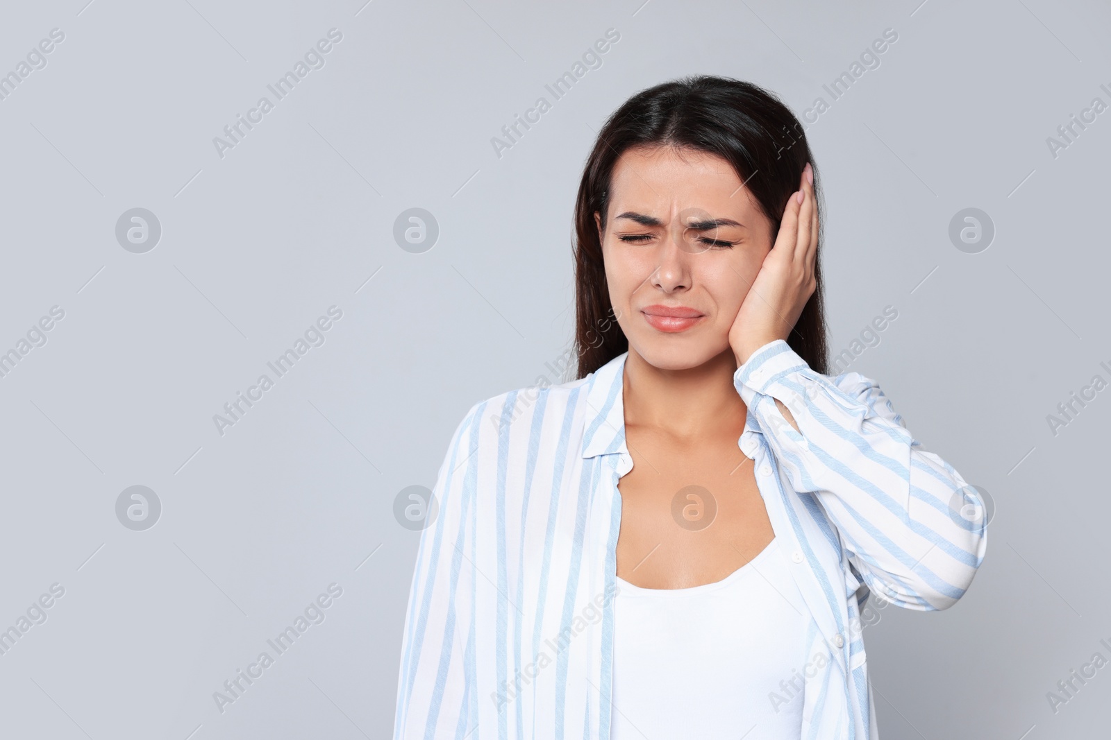 Photo of Young woman suffering from ear pain on light grey background, space for text
