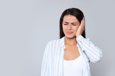 Young woman suffering from ear pain on light grey background, space for text