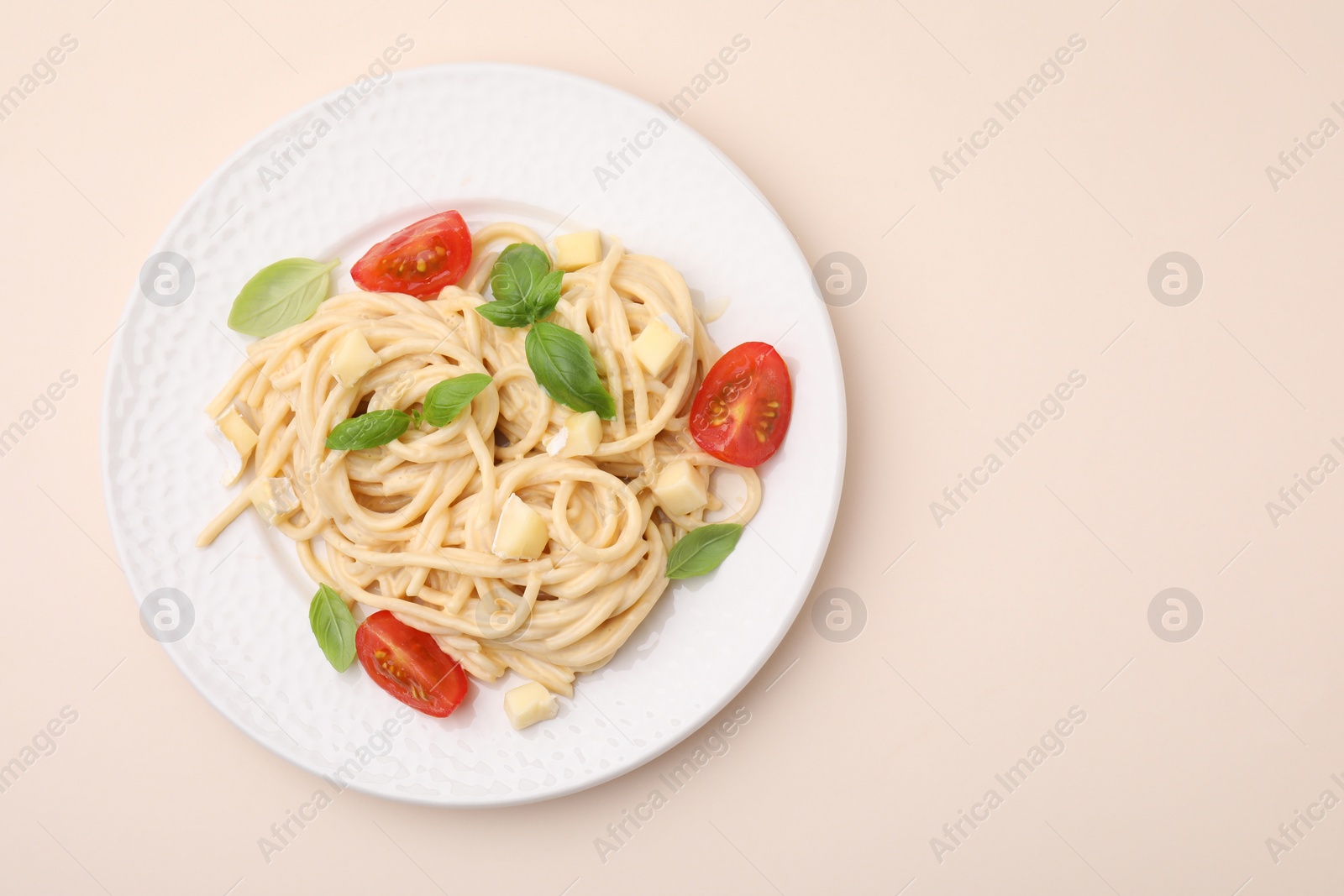 Photo of Delicious pasta with brie cheese, tomatoes and basil leaves on beige background, top view. Space for text