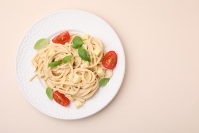 Delicious pasta with brie cheese, tomatoes and basil leaves on beige background, top view. Space for text