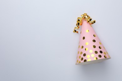 Photo of One pink party hat with serpentine streamers on light background, top view. Space for text