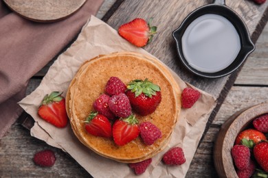 Tasty pancakes served with honey and berries on wooden table, flat lay