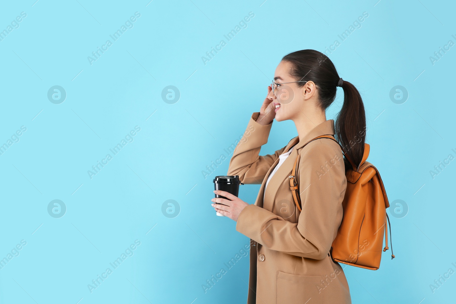 Photo of Beautiful young woman with stylish leather backpack and cup of coffee on turquoise background. Space for text