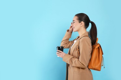 Photo of Beautiful young woman with stylish leather backpack and cup of coffee on turquoise background. Space for text