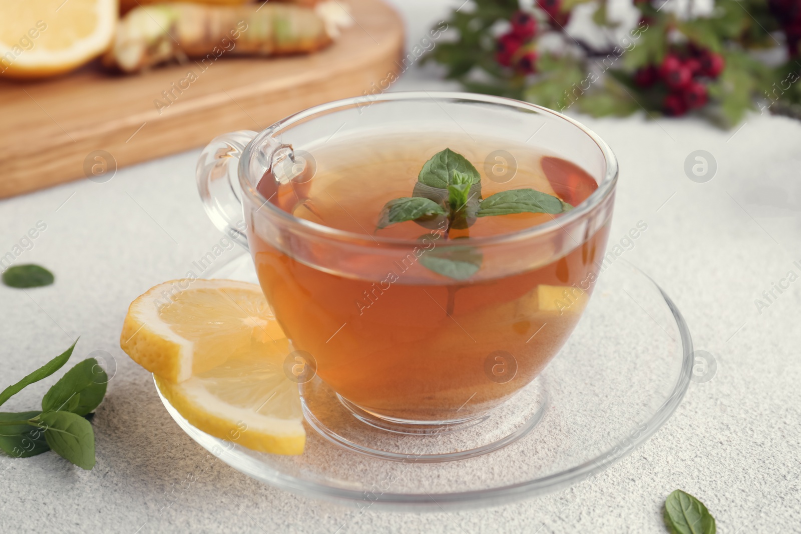 Photo of Glass cup of delicious immunity boosting tea with ingredients on light grey table, closeup