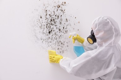 Woman in protective suit and rubber gloves using mold remover and rag on wall