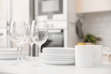 Photo of Stack of clean dishes, glasses and cups on table in kitchen