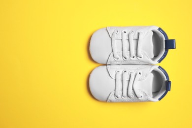 Photo of Cute baby shoes on yellow background, flat lay. Space for text