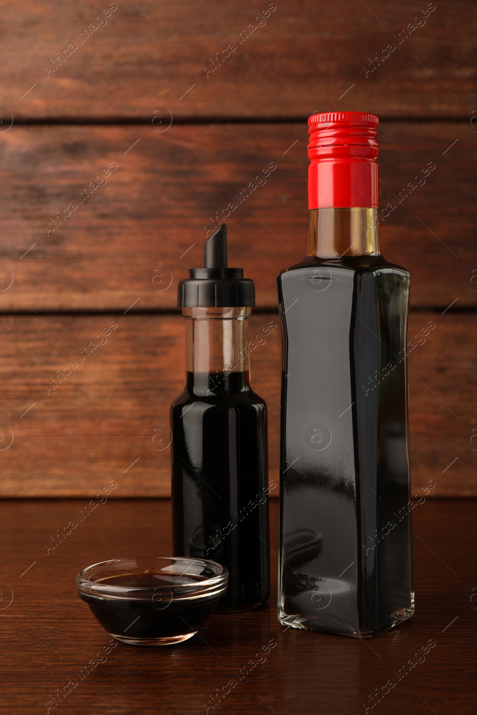 Photo of Bottles and bowl with soy sauce on wooden table