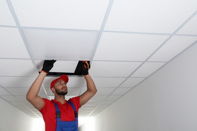 Electrician with pliers repairing ceiling light indoors, space for text