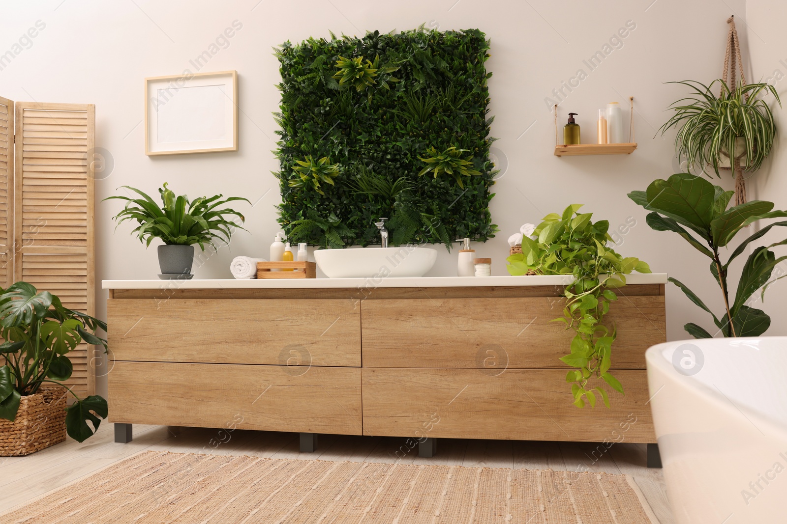 Photo of Green artificial plants, vanity and different personal care products in bathroom