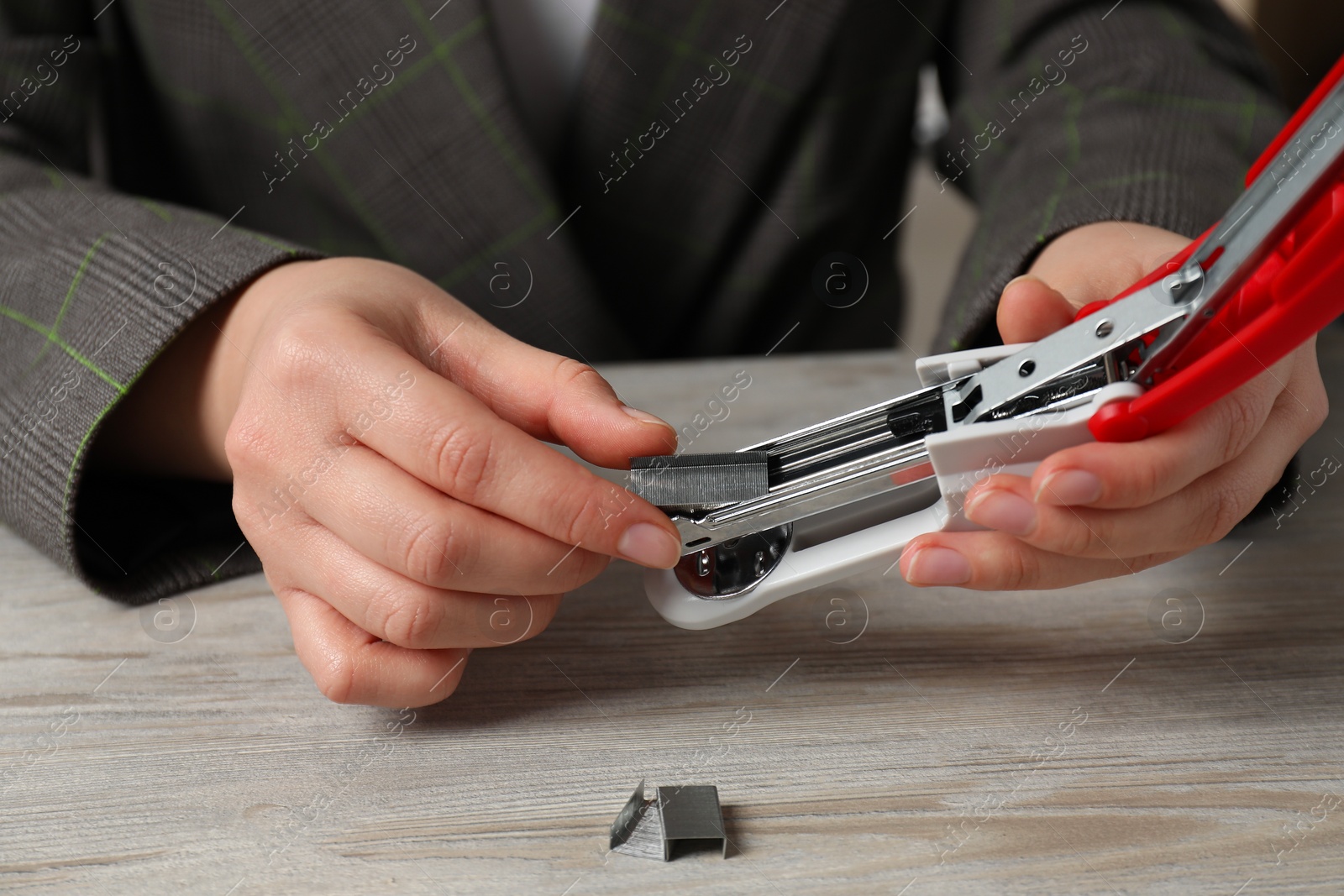 Photo of Woman putting metal staples into stapler at wooden table, closeup