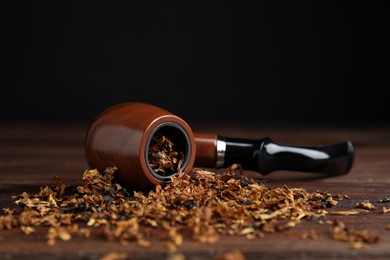 Photo of Smoking pipe and dry tobacco on wooden table against dark background. Space for text