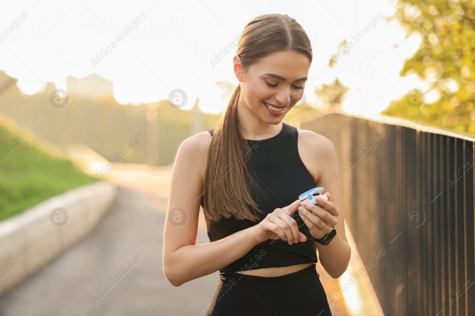 Photo of Happy woman checking pulse with blood pressure monitor on finger after training outdoors. Space for text