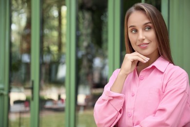Photo of Beautiful young woman in stylish pink shirt near building outdoors, space for text