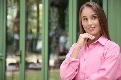 Beautiful young woman in stylish pink shirt near building outdoors, space for text