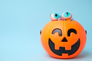 Photo of Halloween trick or treat bucket with different sweets on light blue, space for text