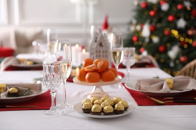 Photo of Christmas table setting with tangerines, candies and dishware indoors