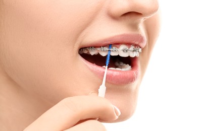 Woman with dental braces cleaning teeth using interdental brush on white background, closeup