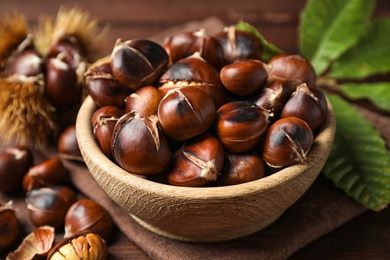 Photo of Delicious roasted edible chestnuts in wooden bowl on table, closeup