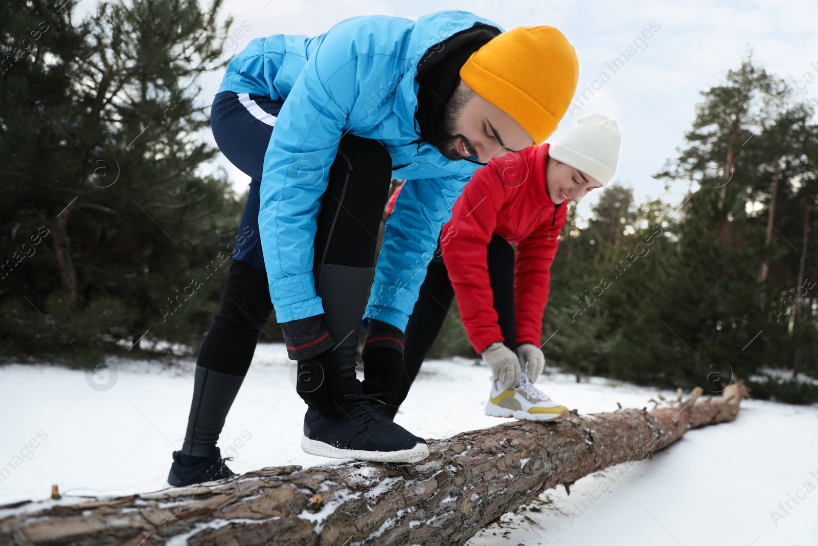 Photo of People lacing sneakers on log in winter forest. Outdoors sports exercises