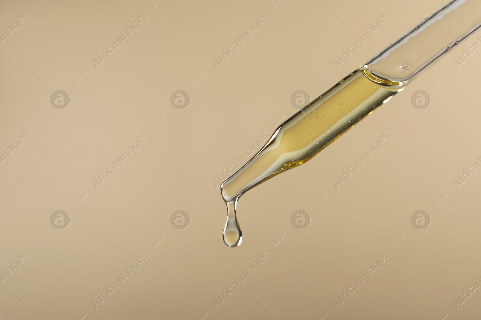 Photo of Dripping hydrophilic oil from pipette on beige background, closeup. Space for text