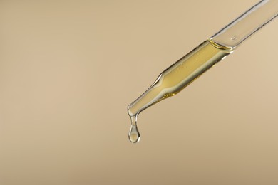 Dripping hydrophilic oil from pipette on beige background, closeup. Space for text