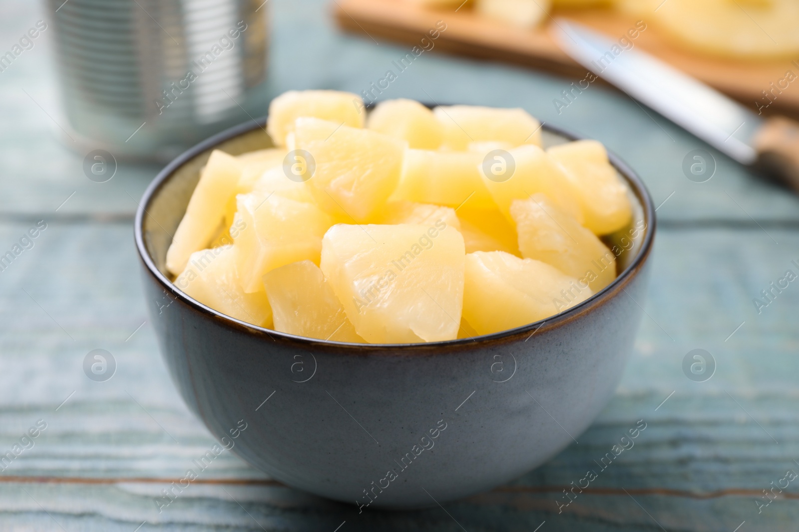 Photo of Pieces of delicious canned pineapple in bowl on light blue wooden table, closeup