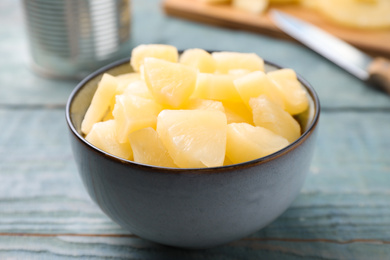 Photo of Pieces of delicious canned pineapple in bowl on light blue wooden table, closeup