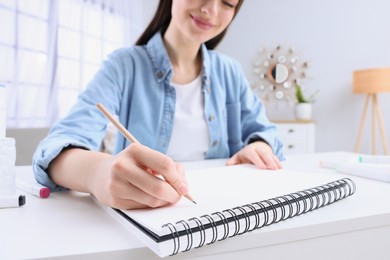 Photo of Young woman drawing in sketchbook at home, focus on hand