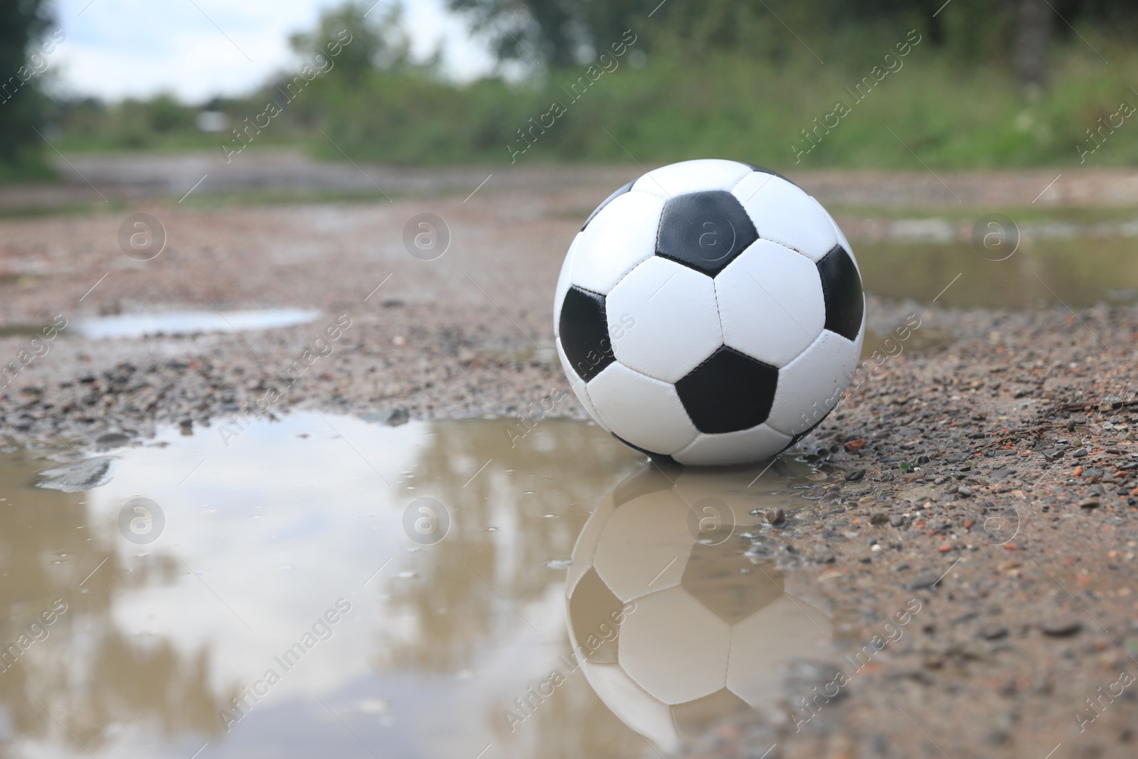 Photo of Soccer ball near puddle outdoors, space for text