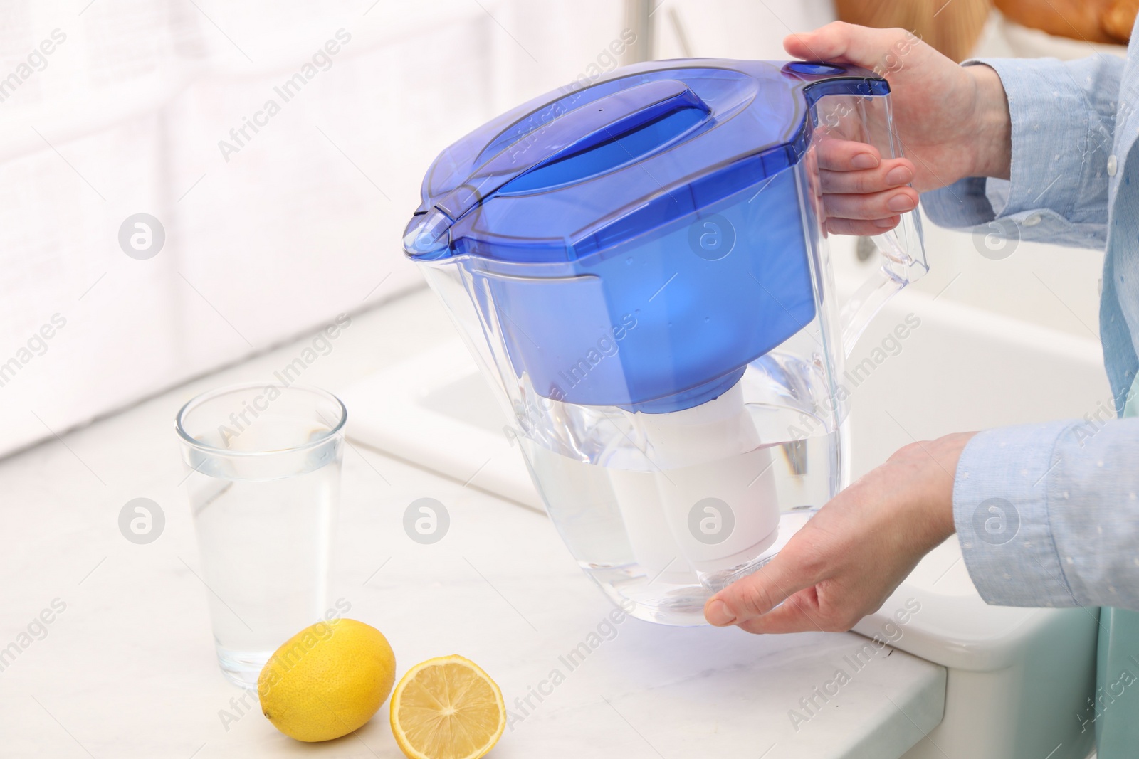 Photo of Woman with water filter jug in kitchen, closeup