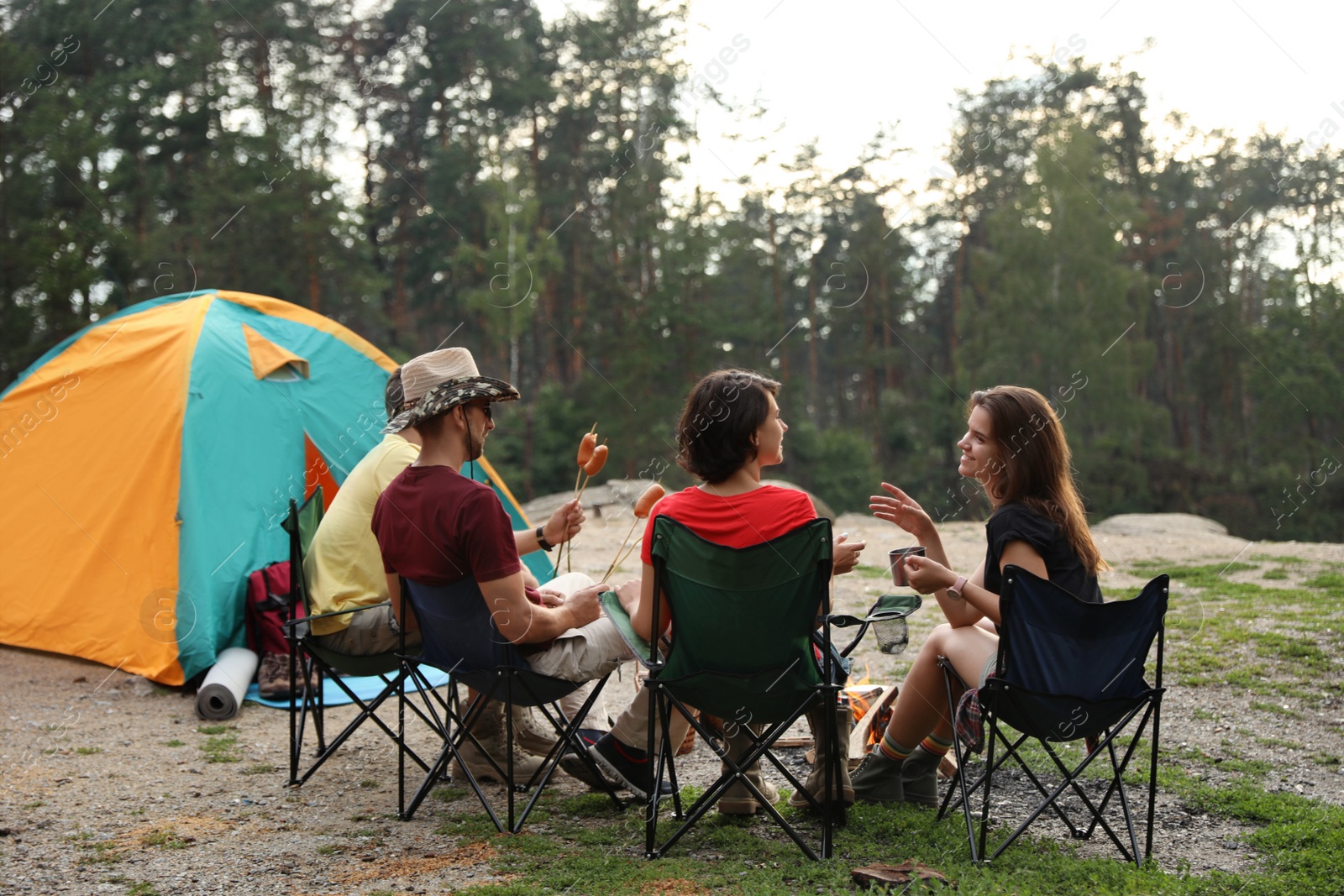 Photo of Young people having lunch with sausages near camping tent outdoors