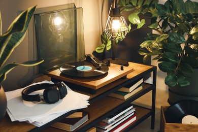 Photo of Stylish turntable with vinyl record on table in cozy room