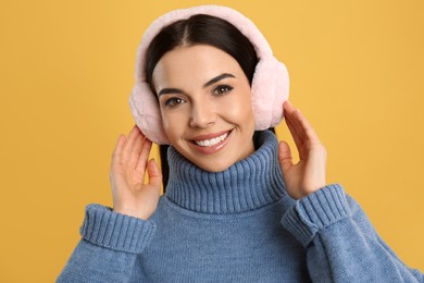 Photo of Beautiful young woman wearing earmuffs on yellow background