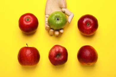 Photo of Mannequin hand with ripe red and green apples on yellow background, flat lay