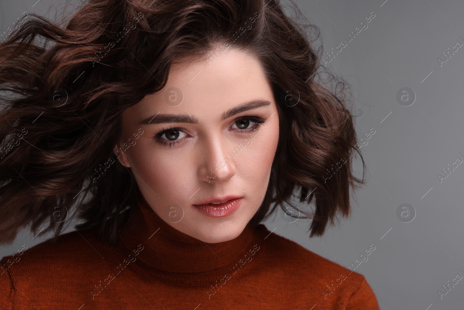 Photo of Beautiful young woman with wavy hairstyle on grey background